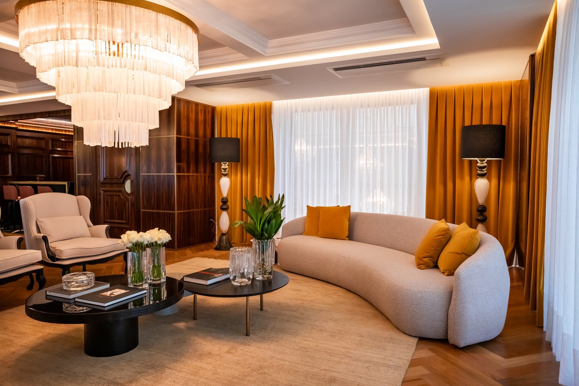 Living decorado do Cartier Residence, com sofá curvo, cortinas em veludo e lustre artesanal