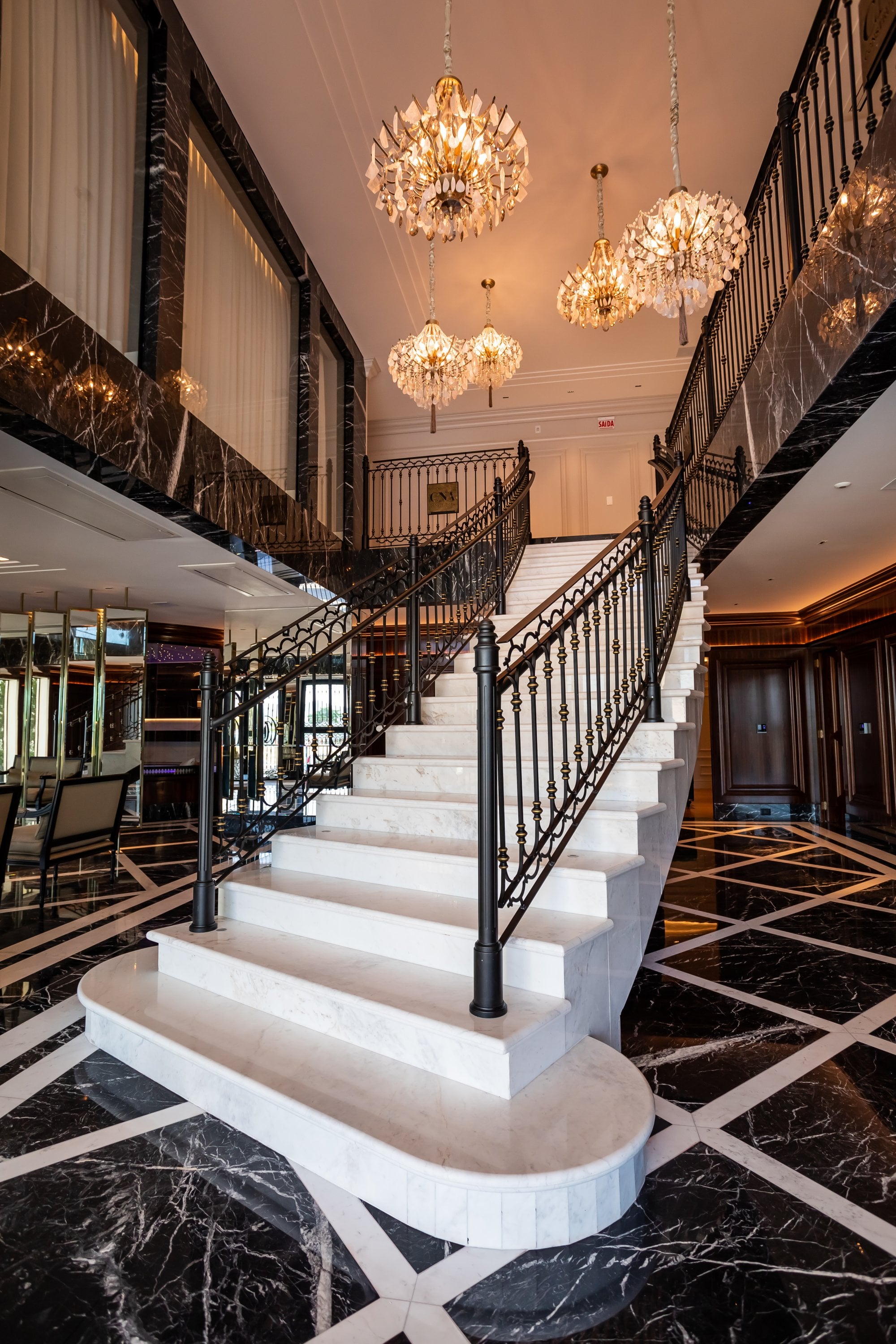 Escadaria de mármore do Cartier Residence, com corrimão de ferro trabalhado e lustres de cristal